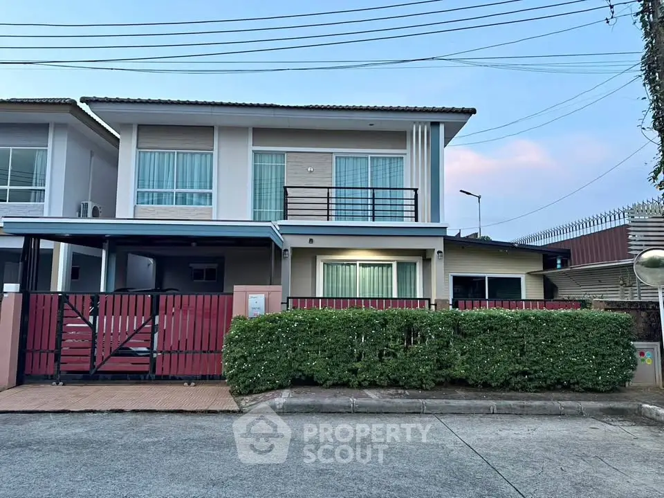 Modern two-story house with gated entrance and manicured hedges in a suburban setting.