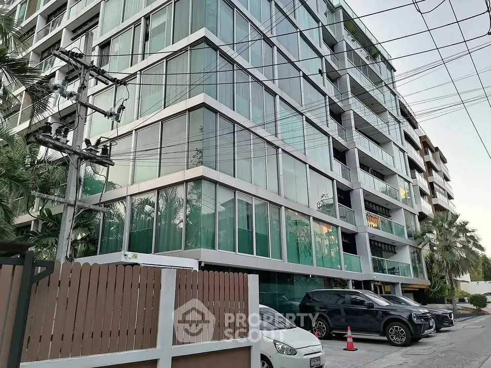 Modern glass facade apartment building with lush greenery and parked cars