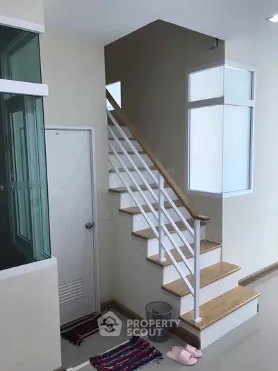 Modern staircase with wooden steps and white railing in a bright interior space.
