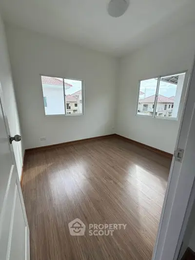 Bright and airy empty room with wooden flooring and large windows in a modern apartment.
