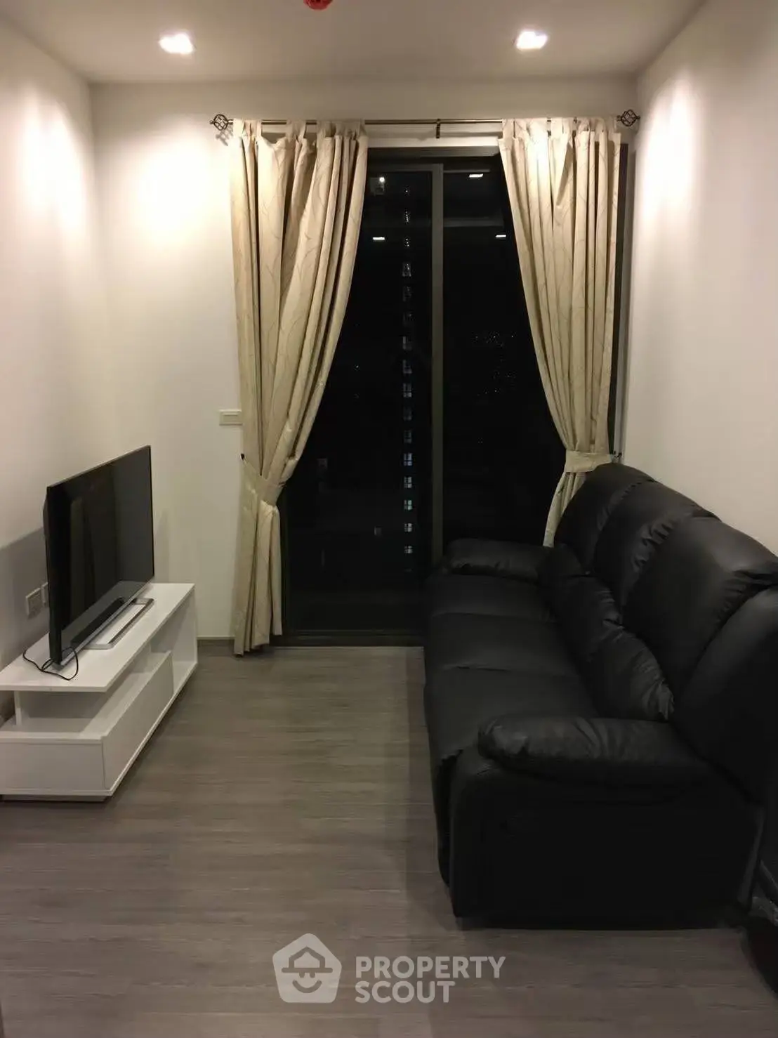 Cozy living room with modern black sofa and sleek TV setup, perfect for relaxation.