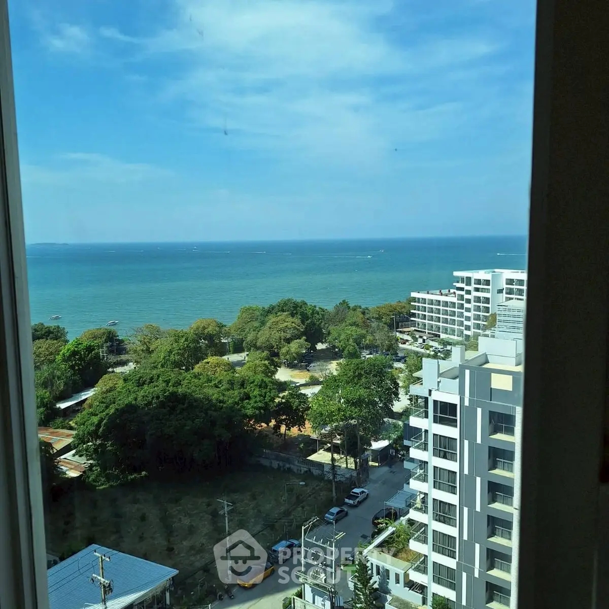 Stunning ocean view from high-rise apartment window, overlooking lush greenery and modern buildings.