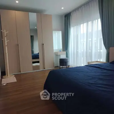 Spacious bedroom with large wardrobe and natural light through sheer curtains.