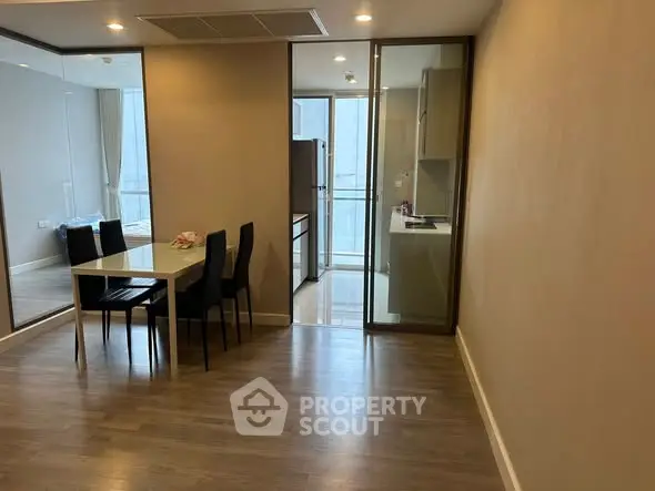 Modern dining area with sleek kitchen and glass partition in a stylish apartment.