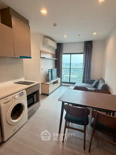 Modern living room with open kitchen and city view balcony, featuring sleek furniture and appliances.