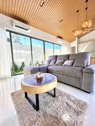 Luxurious modern living room with plush sofa and wooden ceiling, featuring large windows and natural light.