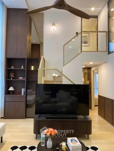 Modern living room with stylish staircase and large TV, featuring elegant wooden accents and contemporary decor.