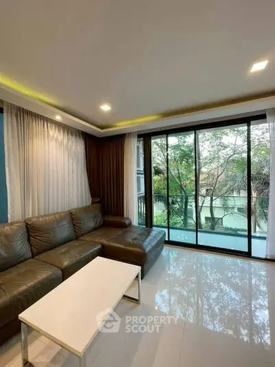 Spacious living room with large windows offering serene garden views, perfect for relaxation and entertaining.