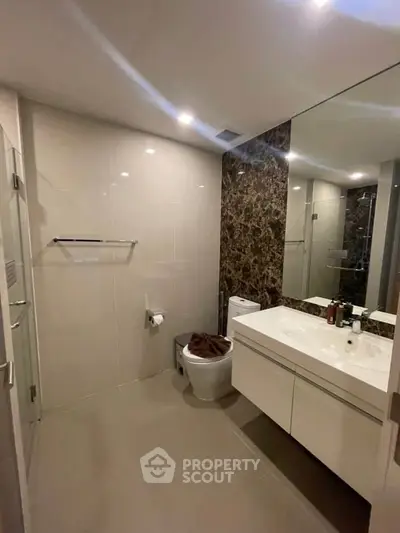 Modern bathroom with sleek design and large mirror, featuring elegant lighting and contemporary fixtures.