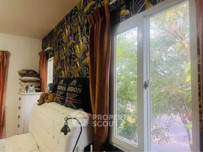 Cozy bedroom with vibrant wallpaper and plush pillows, featuring a large window with a garden view.
