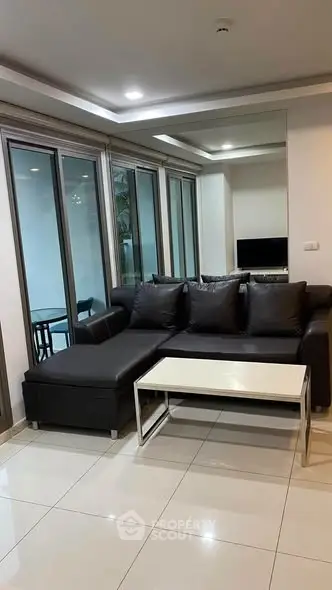 Modern living room with sleek black sofa and glass doors leading to a balcony, perfect for relaxation.