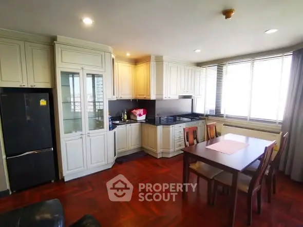 Spacious kitchen with elegant cabinetry and dining area, featuring large windows and hardwood flooring.
