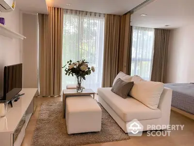 Elegant studio apartment with a plush white sofa, modern decor, and abundant natural light filtering through sheer curtains.