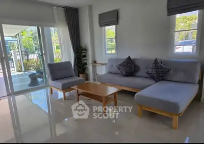 Modern living room with stylish gray furniture and large windows offering natural light and garden view.