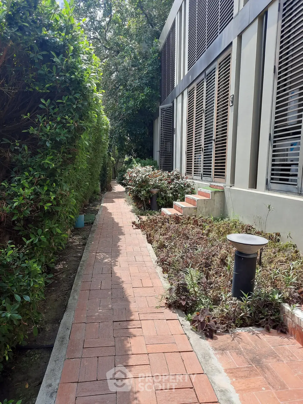 Charming garden pathway leading to a modern building entrance, surrounded by lush greenery.