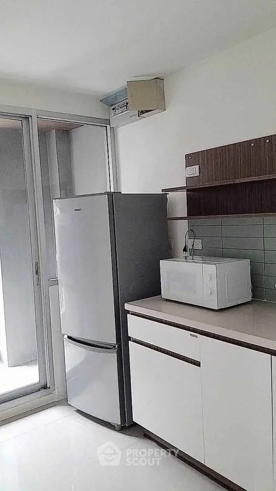 Modern kitchen with sleek cabinets, fridge, and microwave near large window.