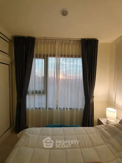 Cozy bedroom with sunset view through large window and elegant curtains.