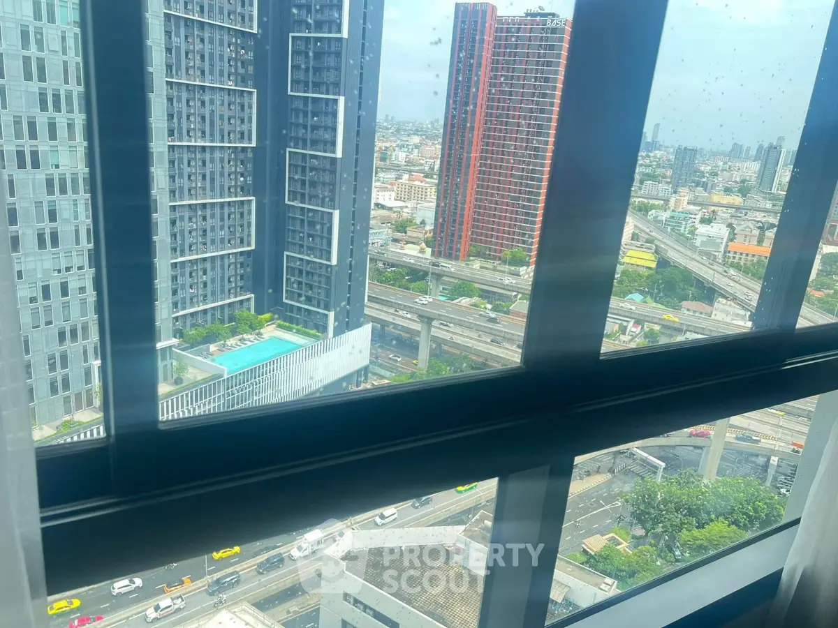 Stunning cityscape view from high-rise apartment window with modern buildings and pool.