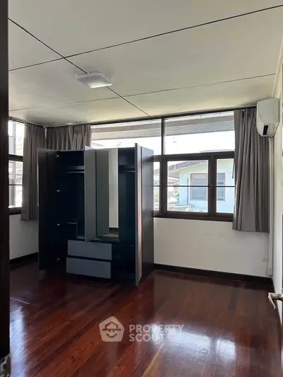 Spacious bedroom with large windows and wooden flooring, featuring a modern wardrobe.