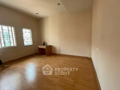 Spacious empty room with wooden flooring and natural light from windows.