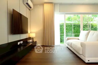 Modern living room with large sofa, flat-screen TV, and garden view through window.