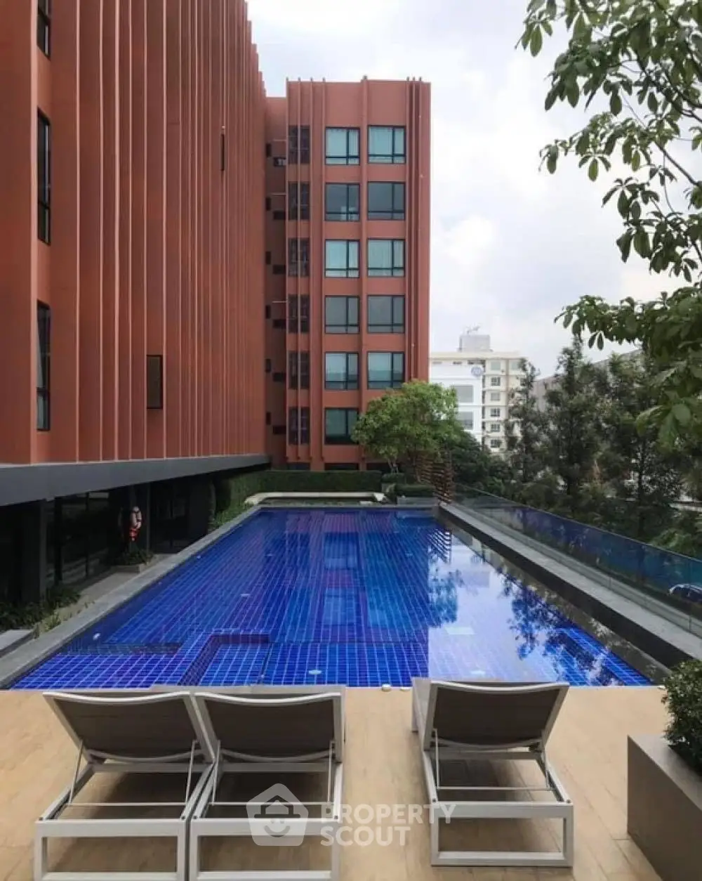 Modern apartment building with luxurious pool and sun loungers in urban setting.