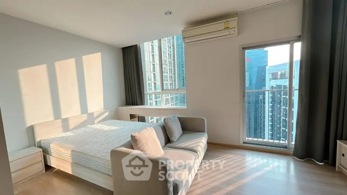Modern bedroom with large windows and city view, featuring a cozy bed and stylish sofa.