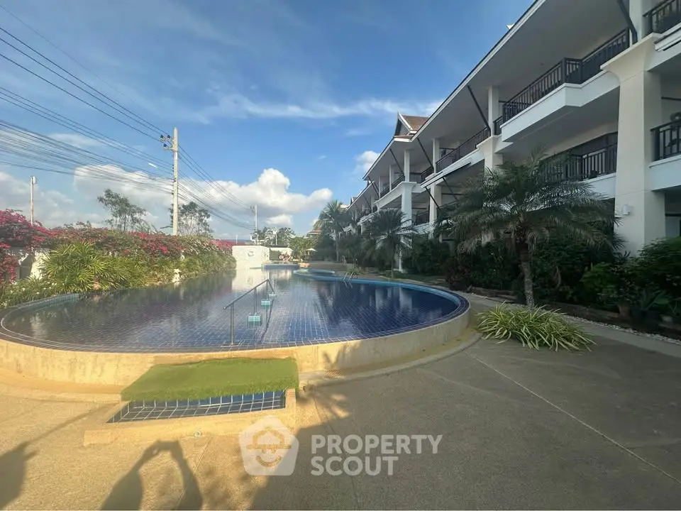 Luxurious apartment complex with stunning pool and lush landscaping under a clear blue sky.