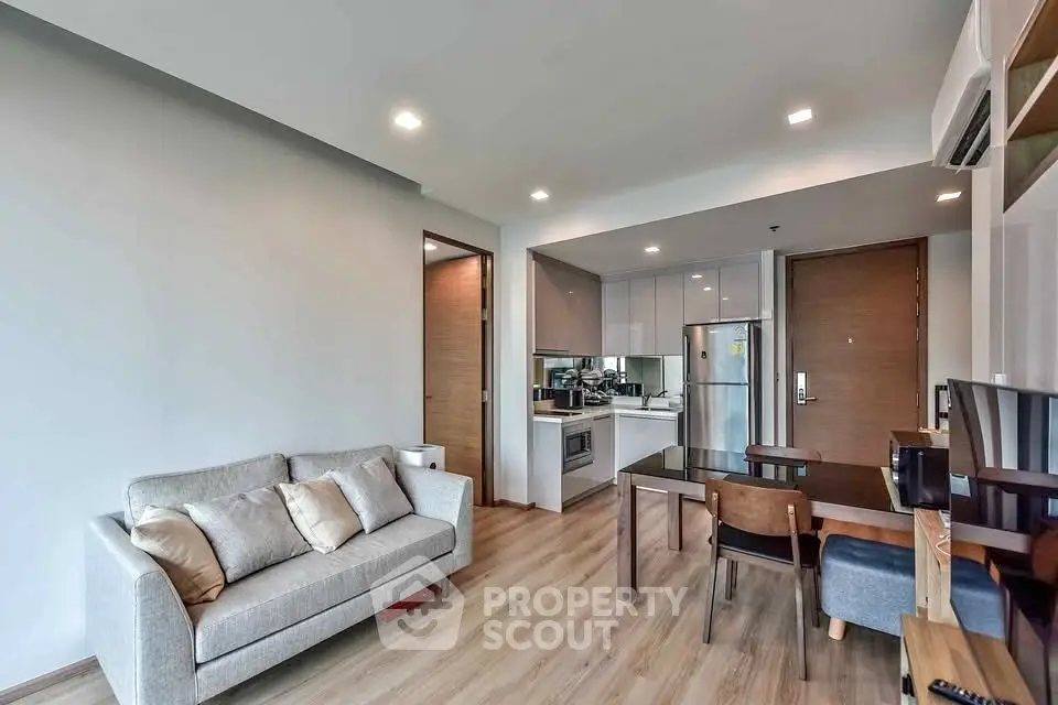 Modern open-layout living room with kitchen, featuring sleek furniture and wooden flooring.