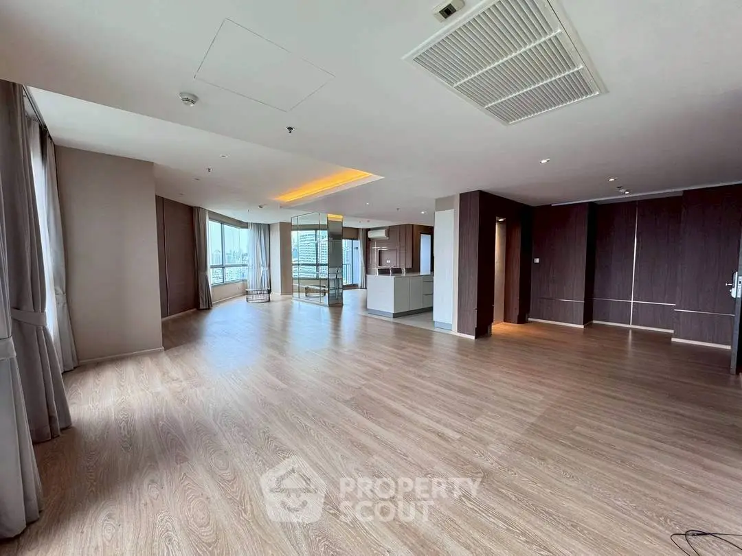 Spacious modern living room with open kitchen and large windows offering city views.