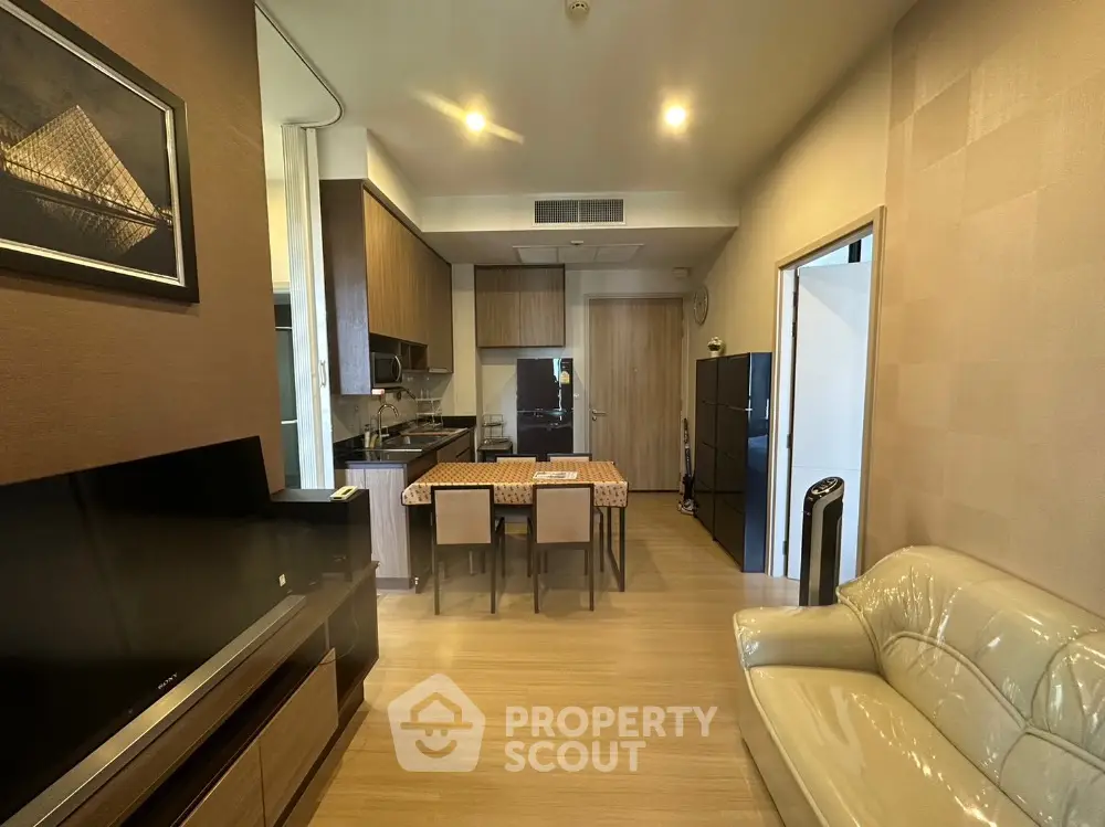Modern open-layout living room with kitchen, featuring sleek furniture and warm lighting.