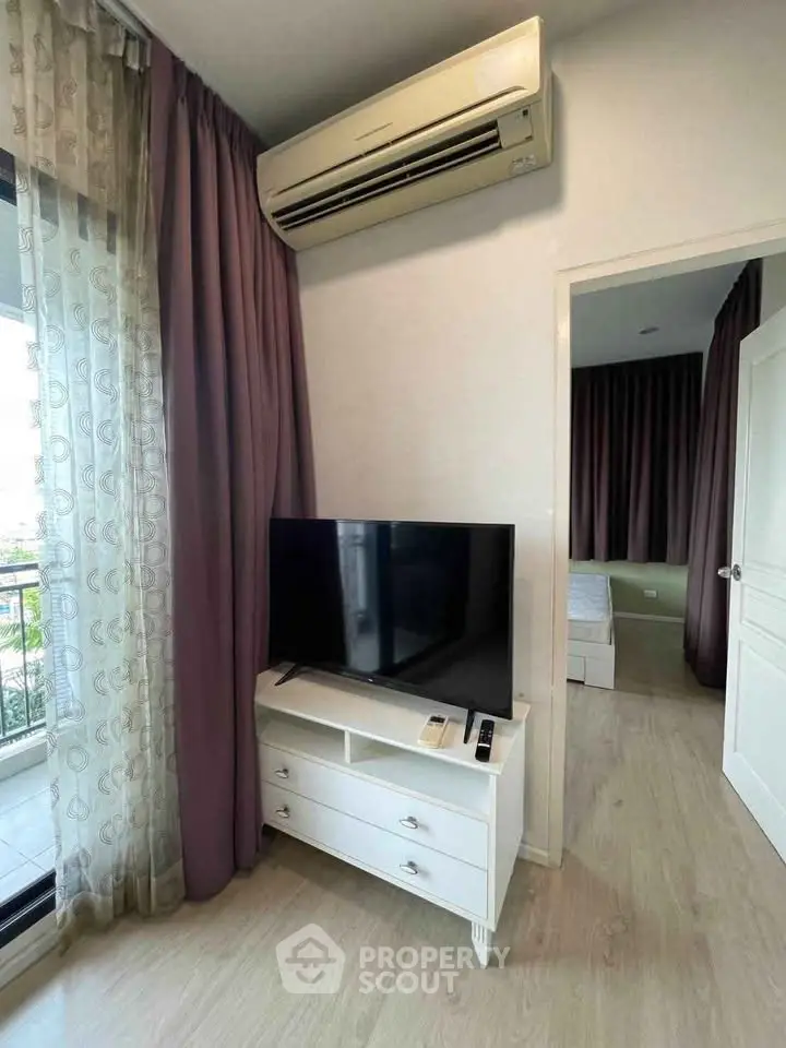 Modern living room with air conditioning and TV, featuring elegant curtains and a glimpse into a cozy bedroom.