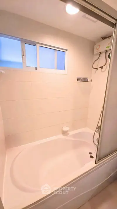 Modern bathroom with bathtub and shower, featuring sleek white tiles and a bright window.