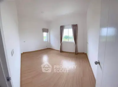 Spacious empty room with wooden flooring and large windows offering natural light.