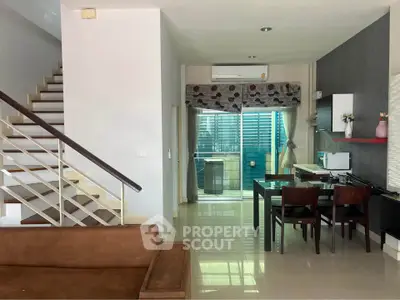 Modern open-plan living area with staircase and dining space, featuring sleek design and natural light.