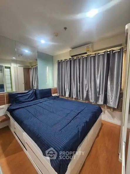 Cozy bedroom with blue bedding and mirrored wall, featuring ample natural light and wooden flooring.