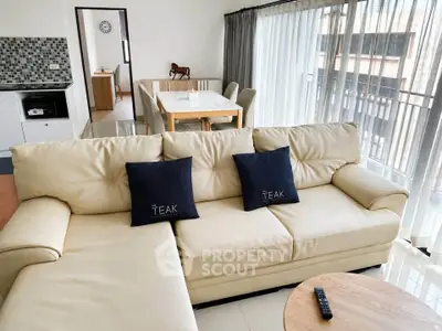 Spacious modern living room with elegant beige sofa and dining area, featuring floor-to-ceiling windows.