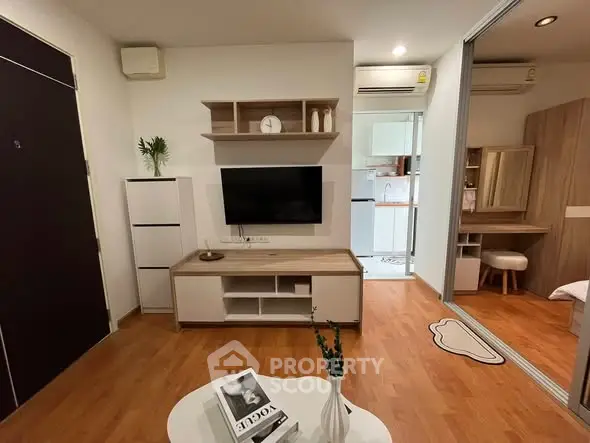 Modern living room with wooden flooring, wall-mounted TV, and stylish decor leading to a cozy kitchen.