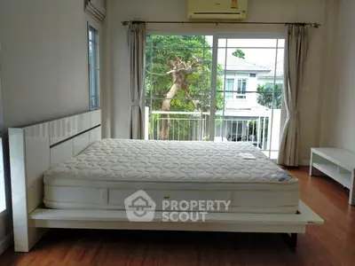 Spacious bedroom with large window and garden view, featuring a modern bed and wooden flooring.