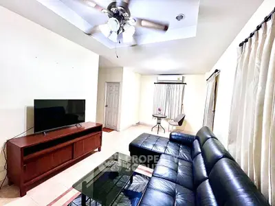 Spacious living room with modern leather sofa and ceiling fan, perfect for relaxation.