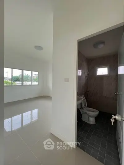 Spacious interior with tiled floors and adjacent bathroom, featuring large windows for natural light.