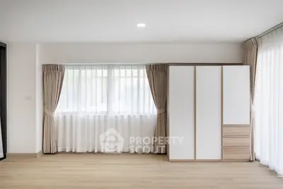 Spacious bedroom with large window and modern wardrobe, featuring elegant curtains and wooden flooring.