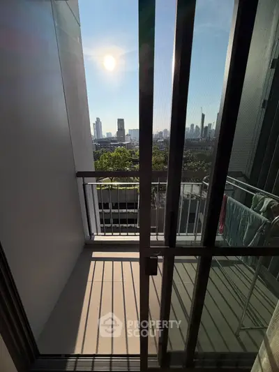 Modern balcony with city skyline view and sunlight streaming through glass doors.