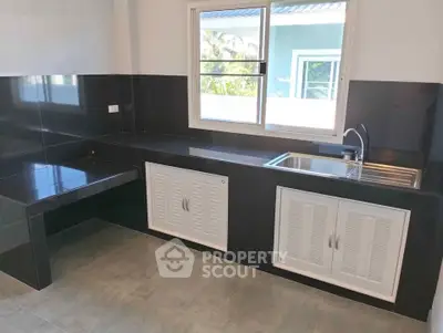 Modern kitchen with sleek black countertops and large window offering natural light.