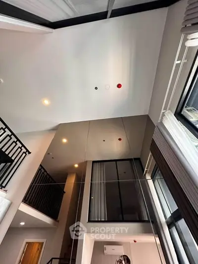 Modern loft interior with high ceilings and large windows, featuring a sleek staircase and contemporary design.