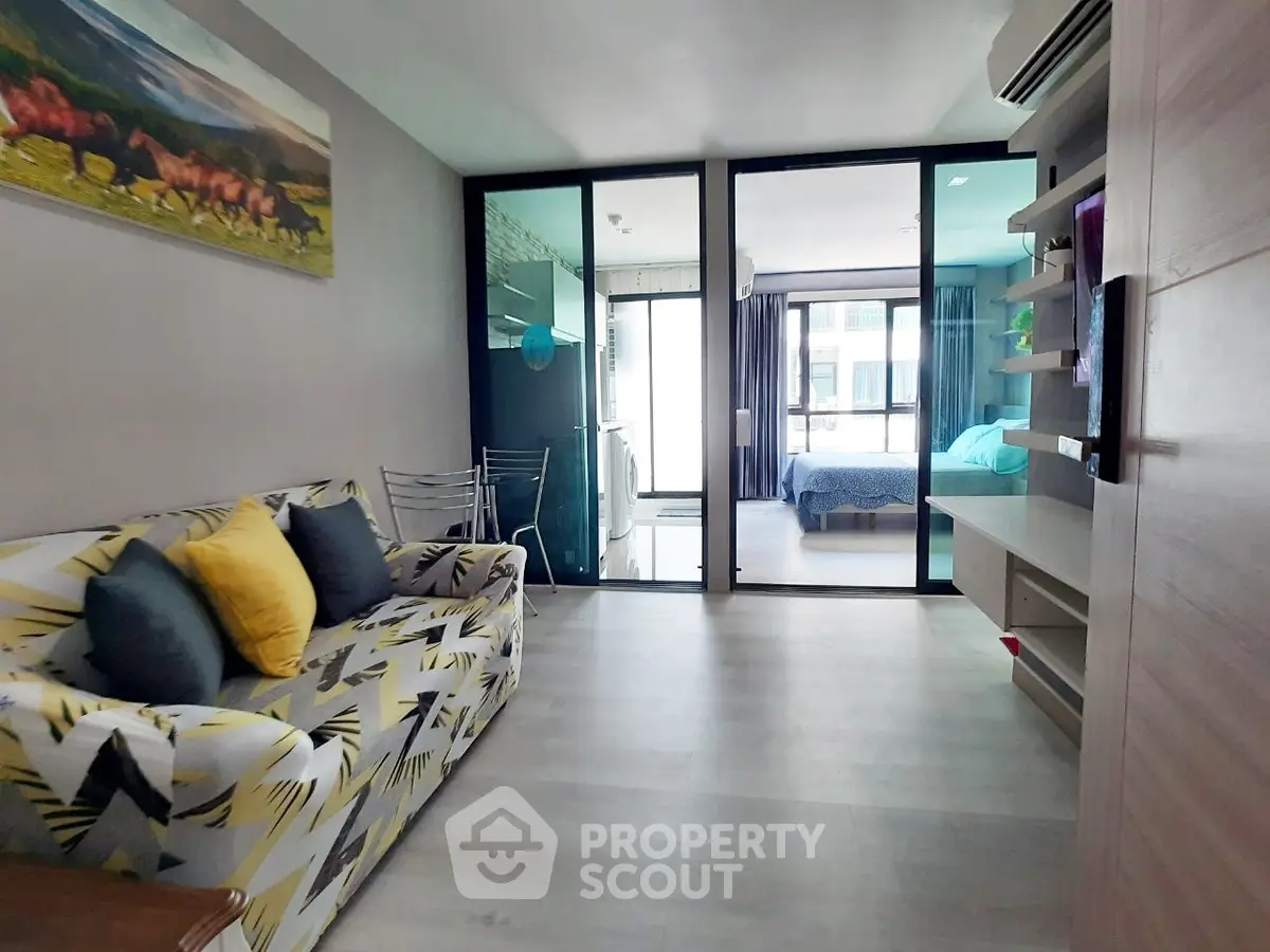 Modern living room with stylish decor and open view to bedroom, featuring vibrant sofa and sleek glass partition.