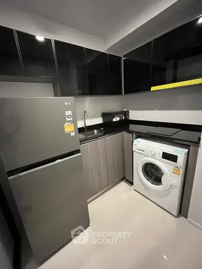 Modern kitchen with sleek cabinets, washing machine, and fridge in compact layout.