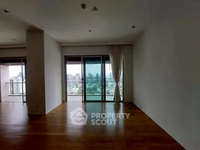 Spacious empty room with large windows offering stunning city view and wooden flooring.