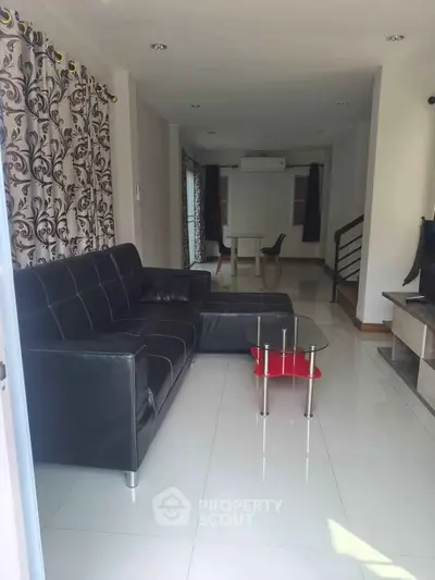 Spacious living room with modern black sofa and elegant curtains, perfect for family gatherings.