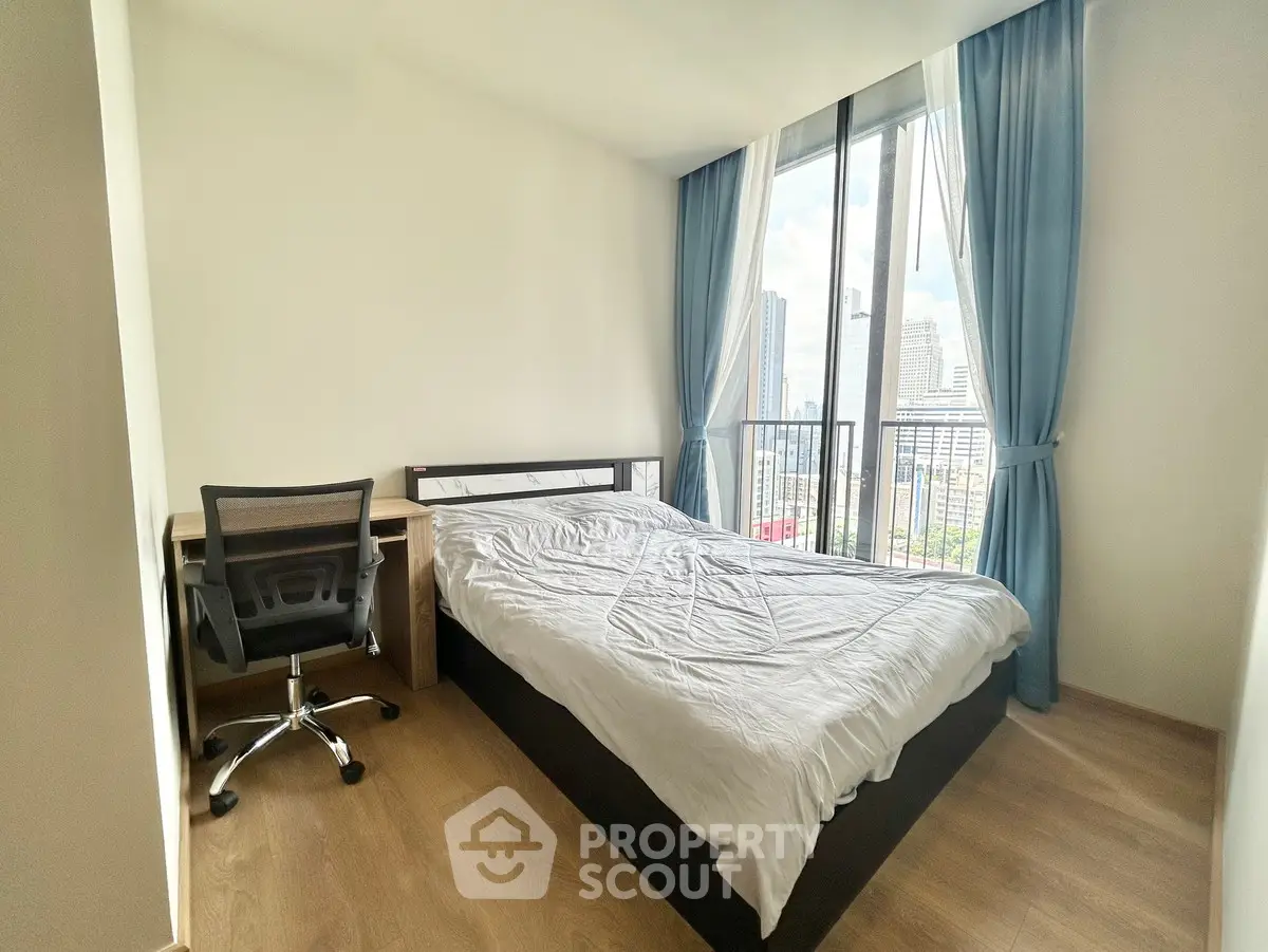 Modern bedroom with city view, featuring a cozy bed and workspace, ideal for urban living.